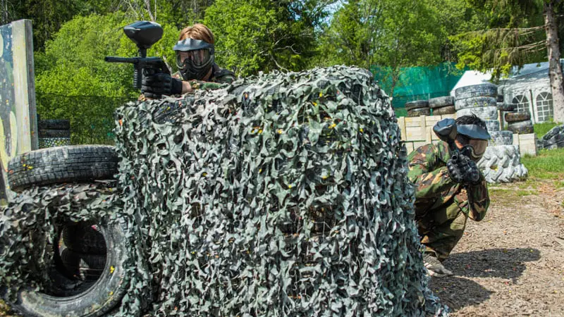 Players behind camouflage cover on the paintball field